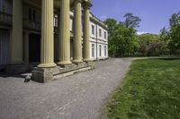 an elegant stone building with two columns and a stone lawn underneath it that has grass growing in the area