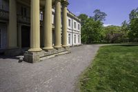 an elegant stone building with two columns and a stone lawn underneath it that has grass growing in the area