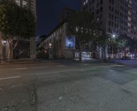 some street with a couple buildings and a lot of light at night time while parked cars are sitting on the street