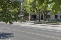 the street is next to a building and some trees in the distance are green leaves