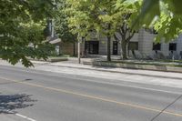 the street is next to a building and some trees in the distance are green leaves