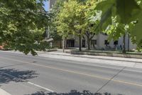 the street is next to a building and some trees in the distance are green leaves