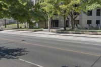 the street is next to a building and some trees in the distance are green leaves