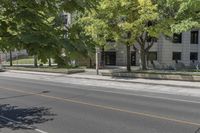 the street is next to a building and some trees in the distance are green leaves