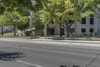 the street is next to a building and some trees in the distance are green leaves