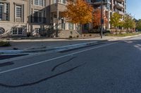 a car is driving on the street next to the apartment complex, with fall foliage