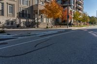 a car is driving on the street next to the apartment complex, with fall foliage