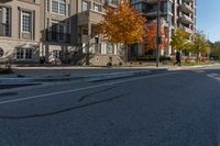 a car is driving on the street next to the apartment complex, with fall foliage