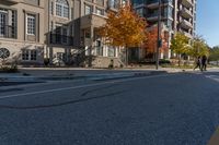 a car is driving on the street next to the apartment complex, with fall foliage