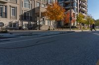 a car is driving on the street next to the apartment complex, with fall foliage