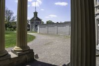 view through some columns of a building with a clock tower in the distance behind it