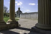 view through some columns of a building with a clock tower in the distance behind it