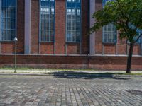 a brick floor sitting outside next to tall windows and a tree on a brick road