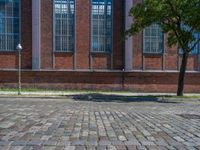 a brick floor sitting outside next to tall windows and a tree on a brick road