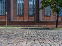 a brick floor sitting outside next to tall windows and a tree on a brick road