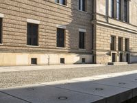 the man walks down the sidewalk by the old brick building as he checks his cell phone