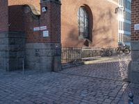 a metal pole sitting next to a brick building with arches on it and an ornate iron gate in front