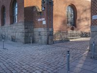 a metal pole sitting next to a brick building with arches on it and an ornate iron gate in front