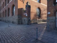 a metal pole sitting next to a brick building with arches on it and an ornate iron gate in front