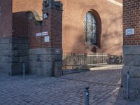 a metal pole sitting next to a brick building with arches on it and an ornate iron gate in front