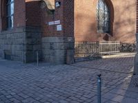 a metal pole sitting next to a brick building with arches on it and an ornate iron gate in front