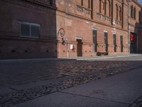 a building with a clock next to the side of it's walls and a person walking by it on a paved sidewalk