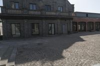 the person is walking down the street near old buildings on a sunny day with a red umbrella