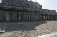 the person is walking down the street near old buildings on a sunny day with a red umbrella