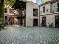 an old brick building with bicycles sitting in the courtyard outside the house and two bikes are parked on the pavement