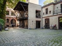 an old brick building with bicycles sitting in the courtyard outside the house and two bikes are parked on the pavement