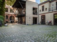 an old brick building with bicycles sitting in the courtyard outside the house and two bikes are parked on the pavement