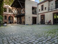 an old brick building with bicycles sitting in the courtyard outside the house and two bikes are parked on the pavement