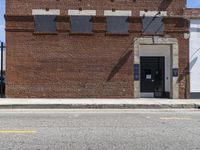 an abandoned brick building sitting across the street from a parked car and a fire hydrant