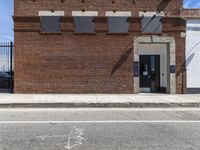 an abandoned brick building sitting across the street from a parked car and a fire hydrant