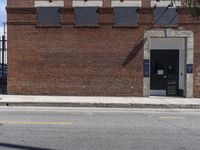 an abandoned brick building sitting across the street from a parked car and a fire hydrant