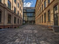 a sidewalk with chairs next to the brick building on the side, some have stairs and some buildings in the background