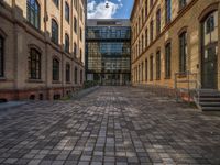 a sidewalk with chairs next to the brick building on the side, some have stairs and some buildings in the background