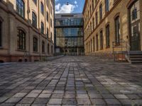 a sidewalk with chairs next to the brick building on the side, some have stairs and some buildings in the background