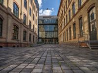 a sidewalk with chairs next to the brick building on the side, some have stairs and some buildings in the background