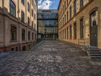 a sidewalk with chairs next to the brick building on the side, some have stairs and some buildings in the background