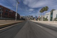 a long city street is shown from the side view mirror of a vehicle as it drives past several palm trees