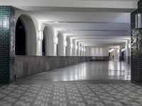 empty, tiled hallway with grey columns and large windows in an indoor facility with tiles on the floor and floor