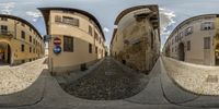 a spherical view is seen here of a narrow street between some tall buildings with cobbles and a red and white sign