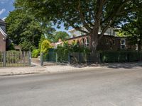 a residential house with a fence surrounding it next to the road and trees on either side of the building