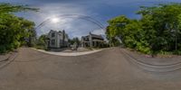 a fish eye view showing the house and road outside in the daytime, with lots of trees surrounding it