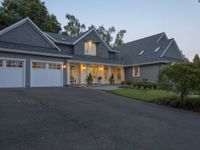 the house is lit up at dusk with a car garage door open on the driveway