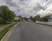 a quiet street lined with residential homes and trees in the foreground is green, grassy land, and houses are in the background