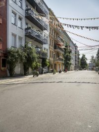 a road lined with parked motor cycles and bunting of festive flags are strung above houses and trees