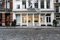 the shop front is white with lots of windows and stairs in front of it that is near a brick street