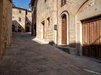 a narrow stone street with wooden doors and brick buildings on either side of the building